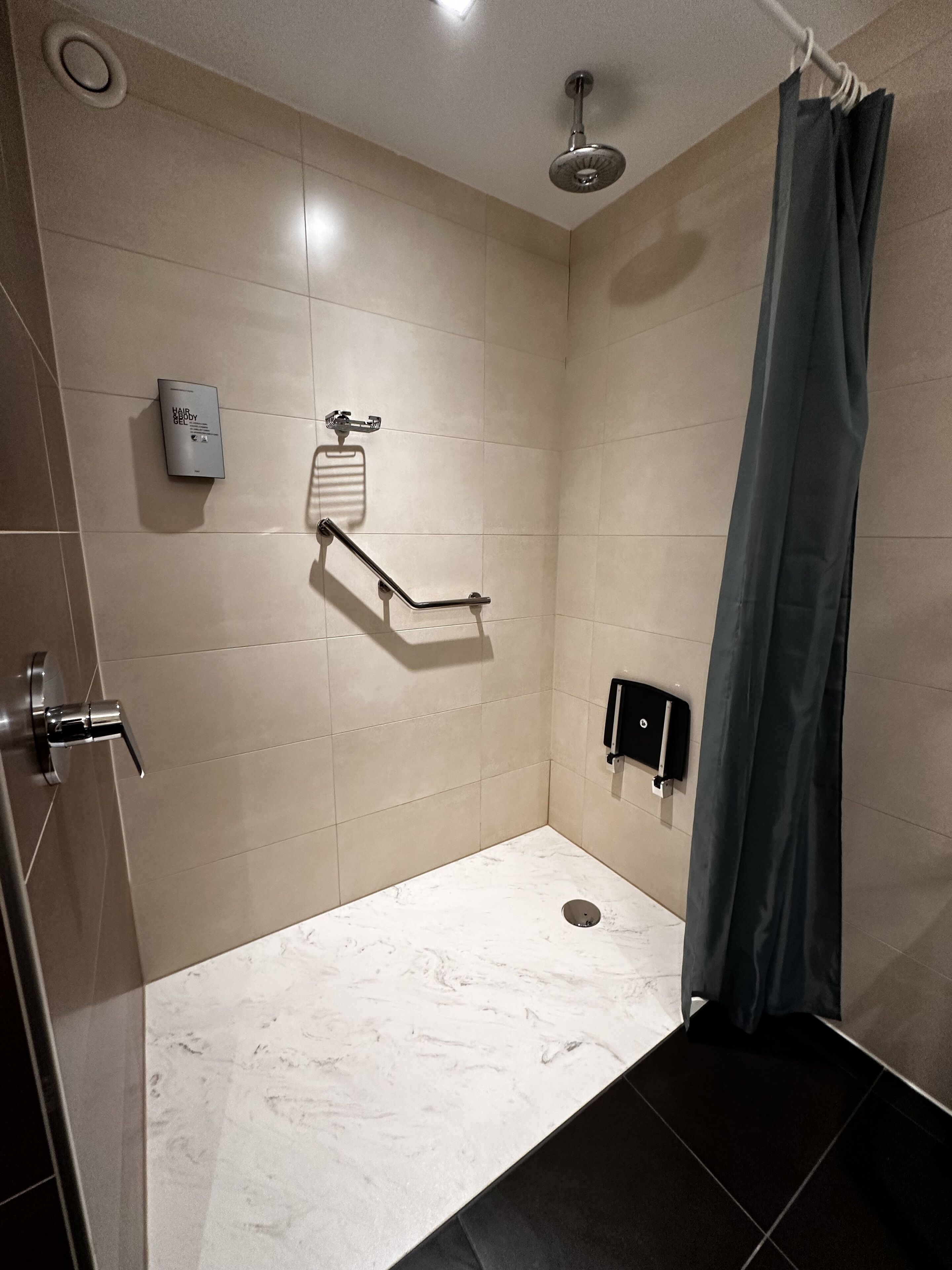 A modern shower with a handheld showerhead, a handheld shower control, and a towel rack.