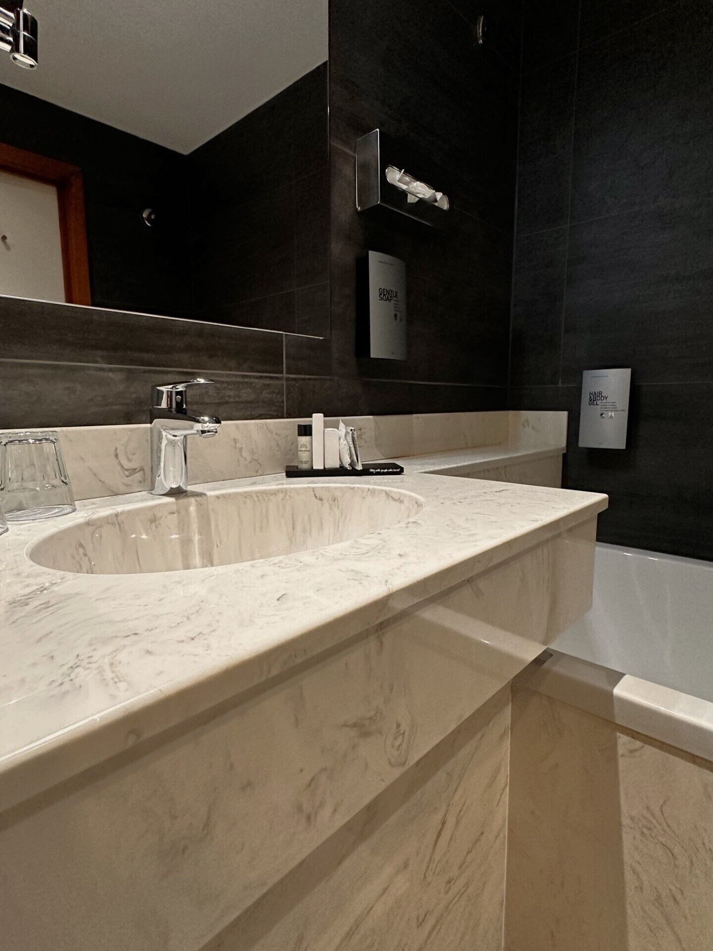 A modern bathroom with a large marble sink, dark walls, and a mirror.