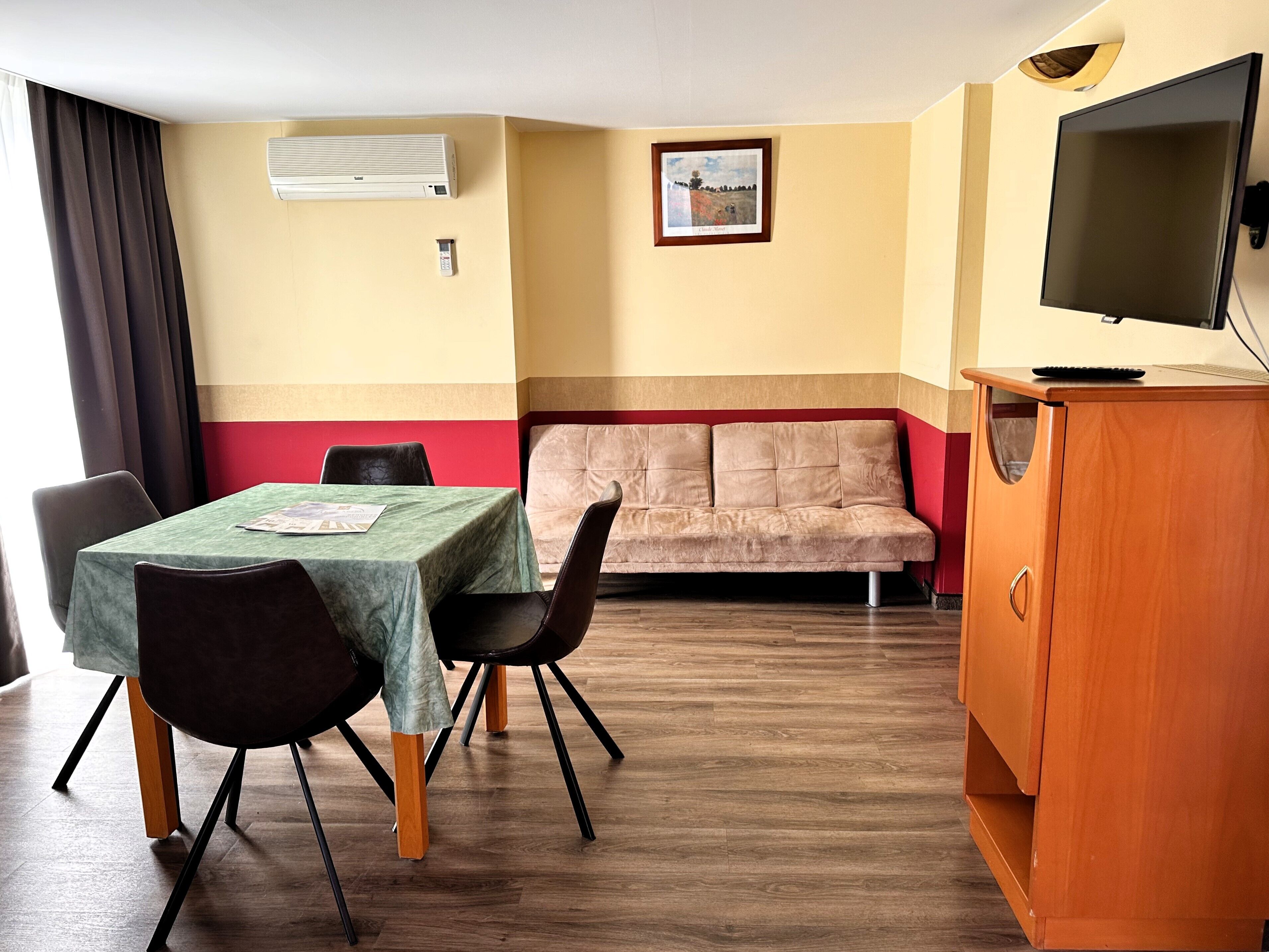 Una habitación con mesa de comedor, sillas, un sofá, televisor y aire acondicionado.