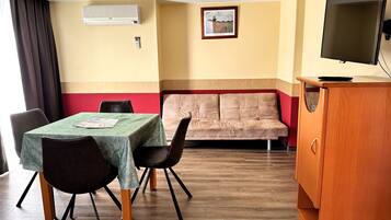 Una habitación con mesa de comedor, sillas, un sofá, televisor y aire acondicionado.