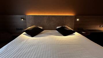 Een hotelkamer met een groot bed, twee zwarte kussens, een houten hoofdbord en wandlampen.