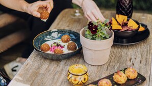 A person serving food at an outdoor table with a variety of dishes and drinks. - Hotel Melba (Bastogne)