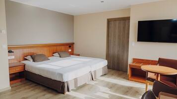 A hotel room with a double bed, a wooden nightstand, a desk with a chair, a television on the wall, and a wooden door.