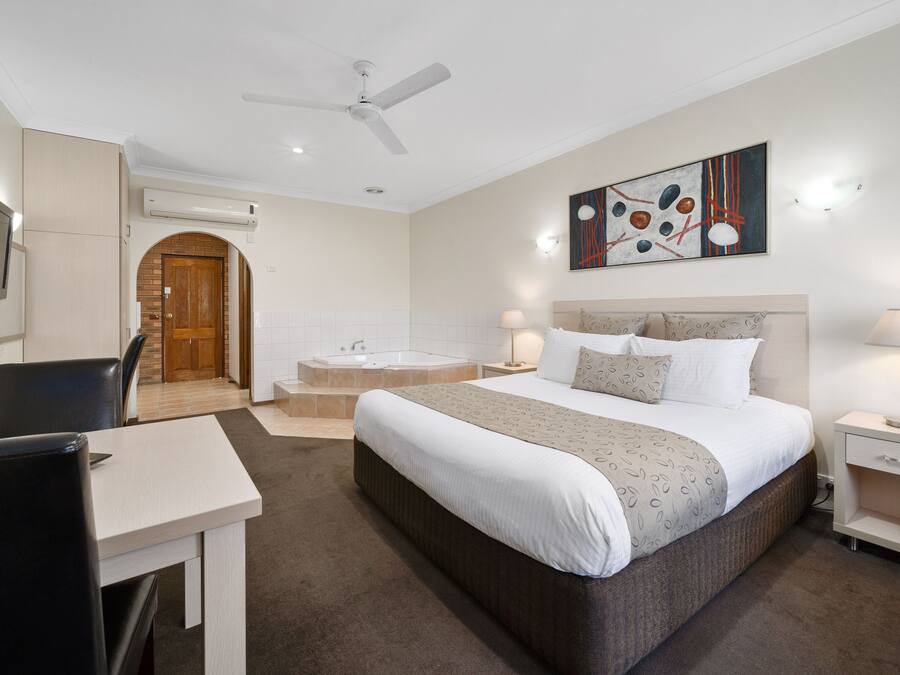 Una camera d'albergo con un letto, una scrivania, una sedia, una televisione, una ventola a soffitto e un bagno con vasca e doccia.