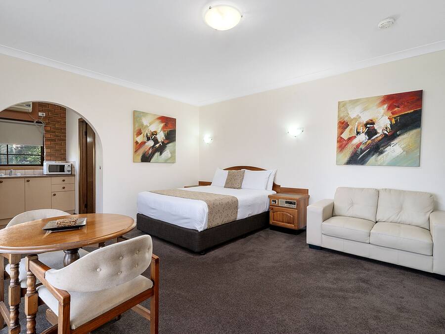 A hotel room with a bed, a sofa, a dining table, and a kitchen area visible through an archway.