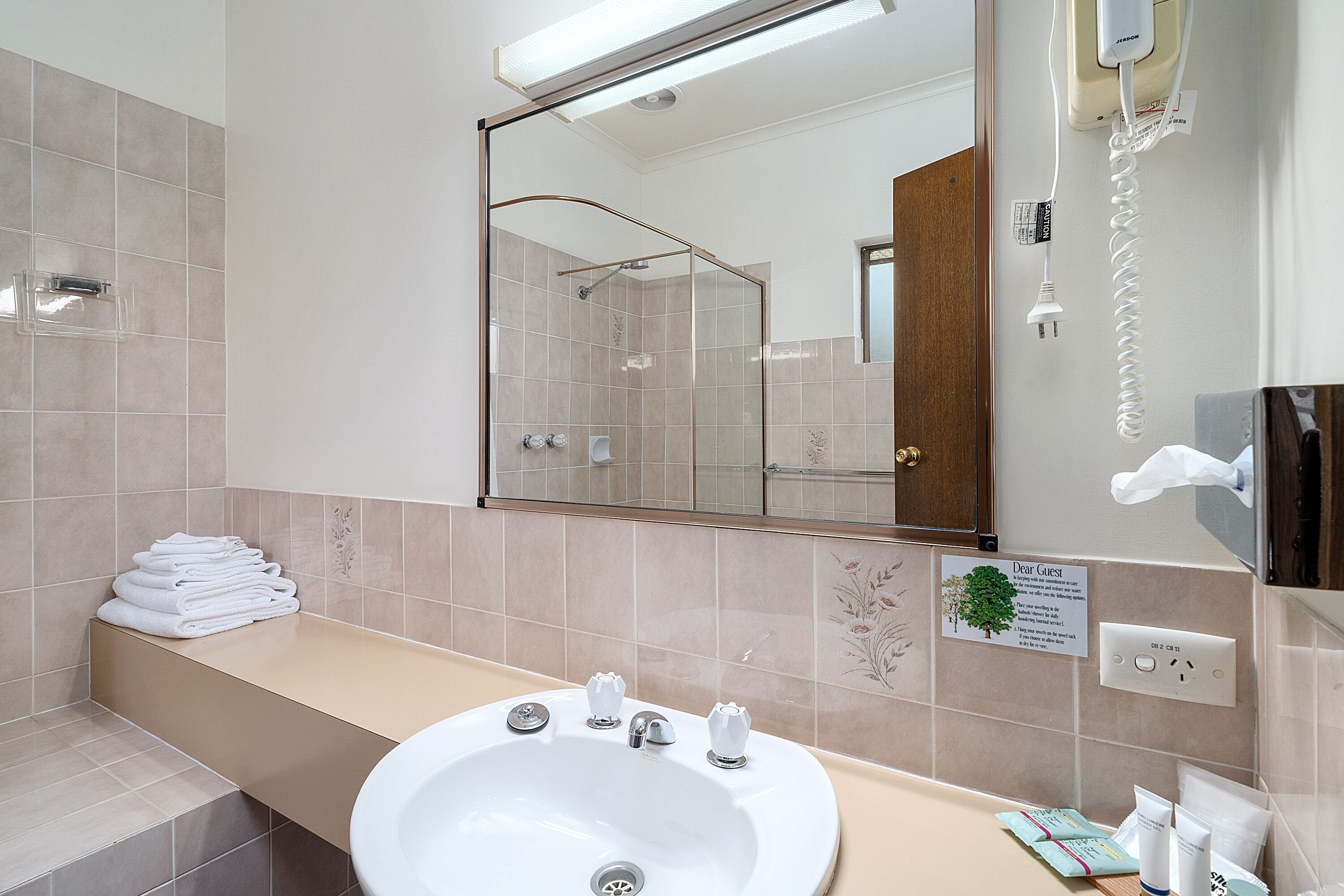 Ein Hotelbad mit Waschbecken, Spiegel und einem Stapel weißer Handtücher.