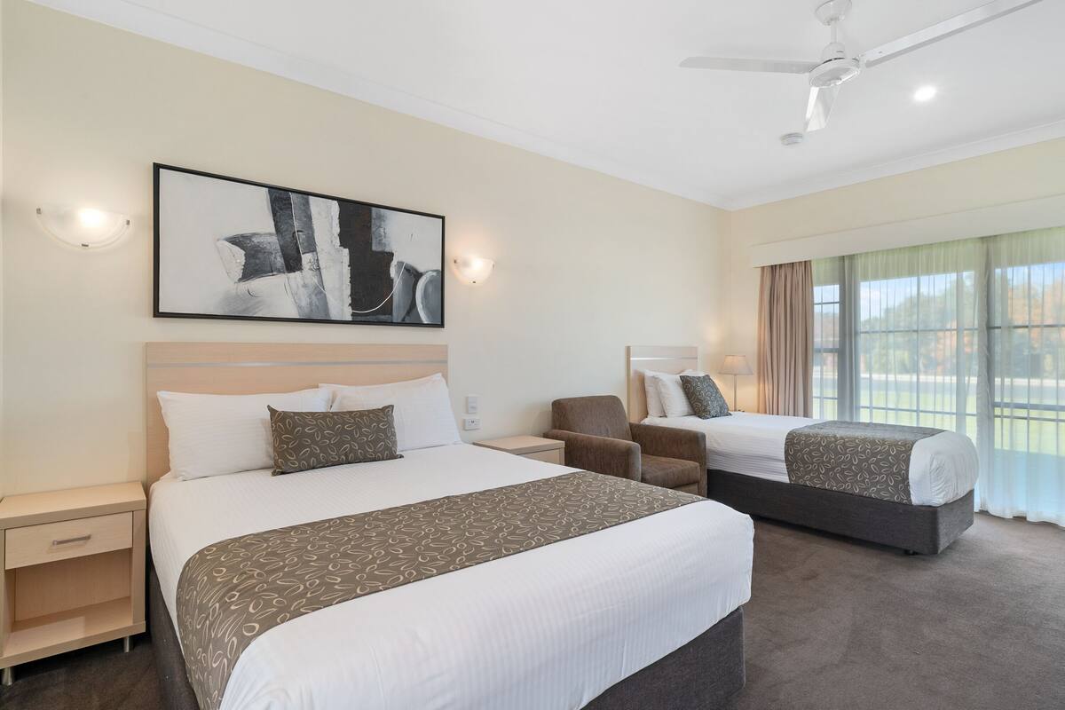A hotel room with two beds, a chair, a nightstand, and a ceiling fan.