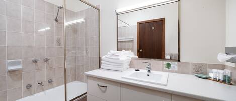 Un baño moderno con ducha de vidrio, lavamanos con espejo y una pila de toallas blancas en la encimera.