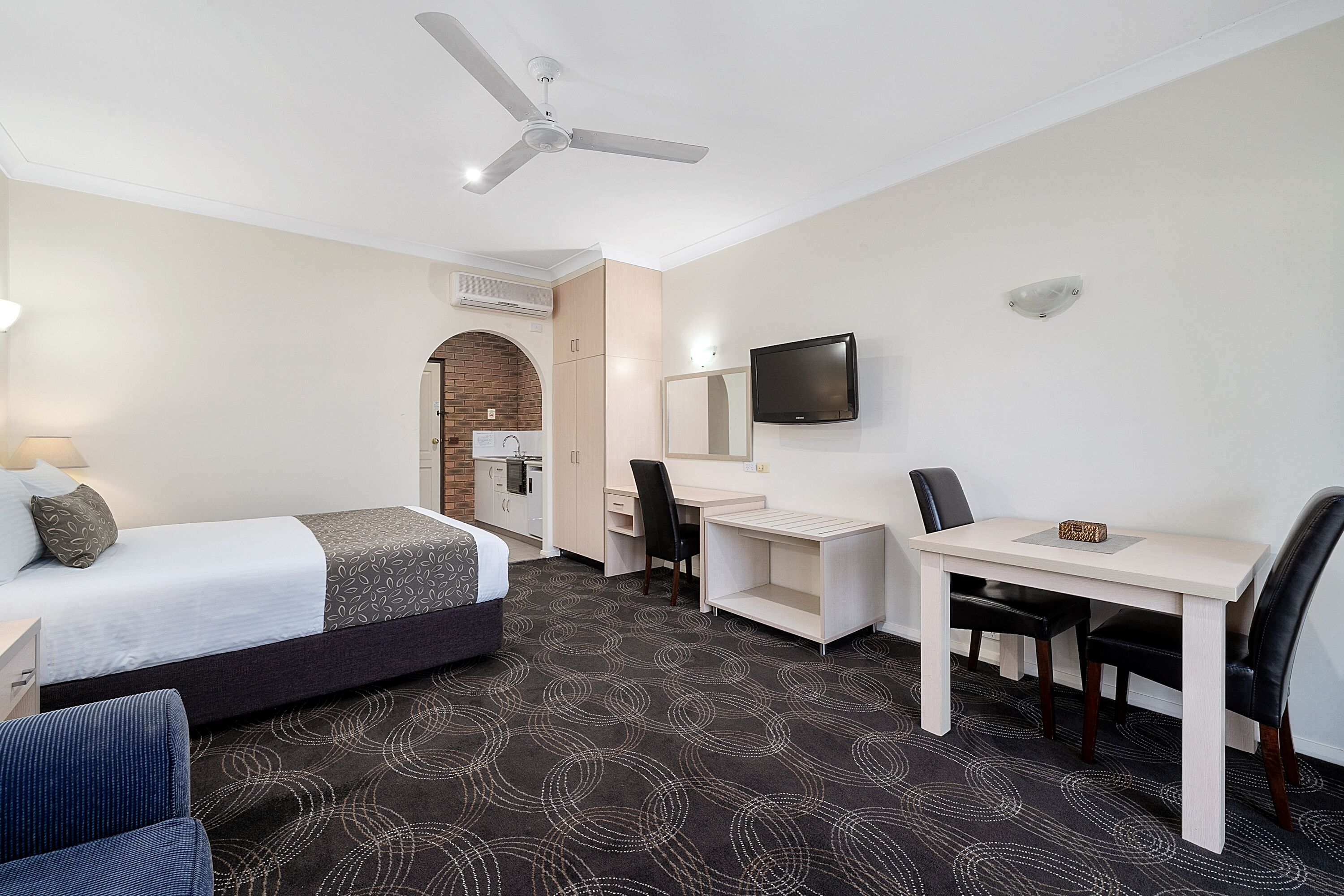 Habitación de hotel con cama, escritorio, silla, televisor y ventilador de techo.