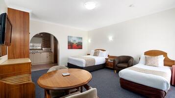 A hotel room with two beds, a dining table, a TV, and a kitchenette.