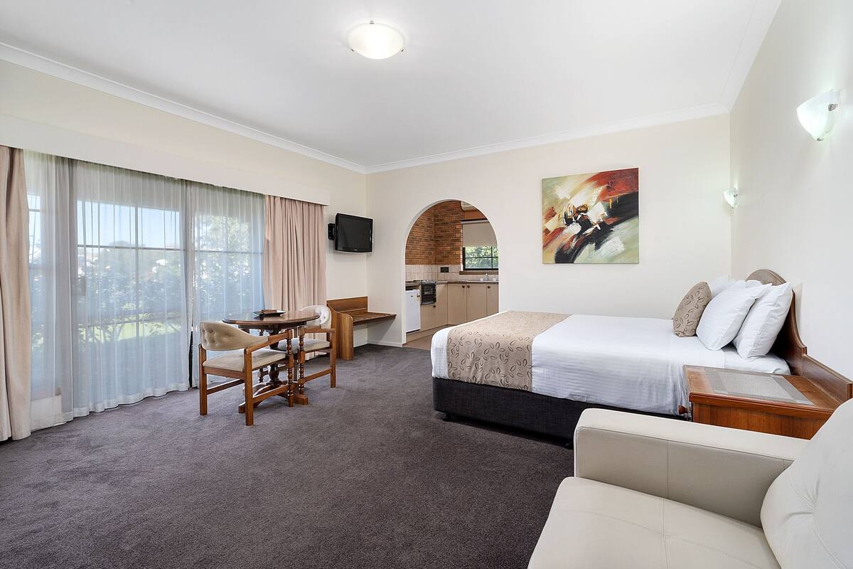 A hotel room with a bed, a desk, a chair, a sofa, a TV, and a painting.
