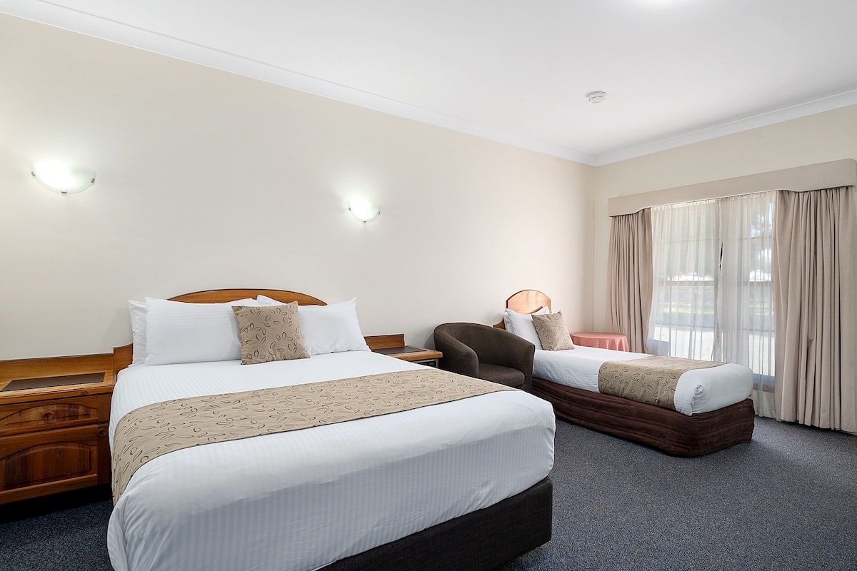 A hotel room with two beds, a wooden nightstand, a chair, and a window with curtains.