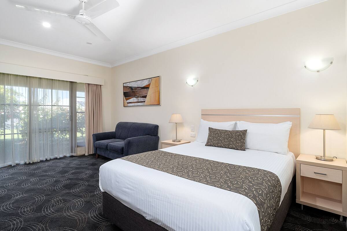 A hotel room with a bed, a chair, a nightstand, a lamp, and a ceiling fan.
