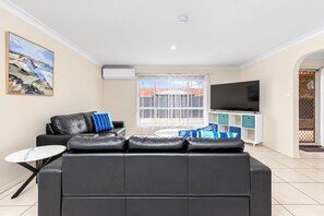 A modern living room with a black leather sofa, a small round table, a flat-screen TV, and a window with blinds. - Best Western Ambassador Motor Inn & Apartments (Wagga Wagga)
