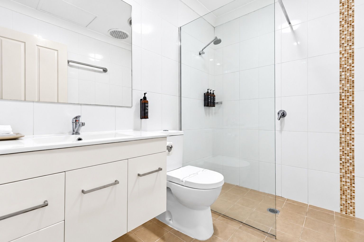 Un baño moderno con lavamanos, espejo e inodoro blancos.