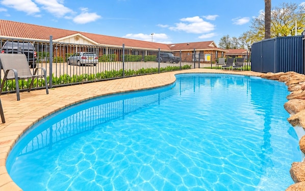 A swimming pool with a tiled deck, surrounded by a fence and a building with a tiled roof.