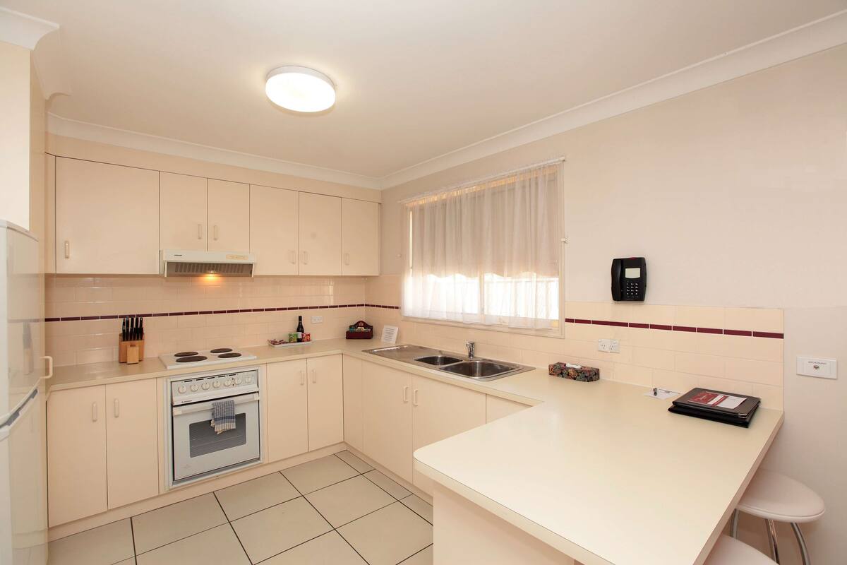 A modern kitchen with white cabinets, a built-in oven, a sink, and a window with sheer curtains.