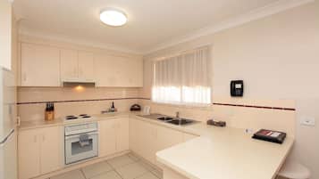 A modern kitchen with white cabinets, a built-in oven, a sink, and a window with sheer curtains.