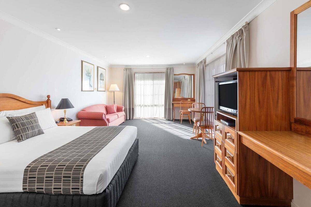 A hotel room with a bed, a desk, a TV, a sofa, and a dining area.