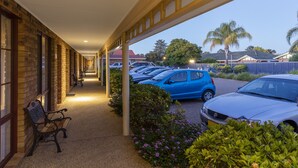 Uma galeria coberta com bancos, uma área de estacionamento com carros, e um edifício com paredes de tijolo e janelas.