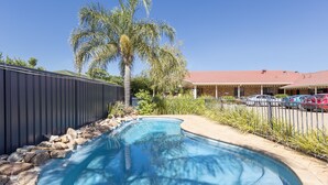 Piscina com borda curva, cercada por um limite de pedra e uma grade de metal.