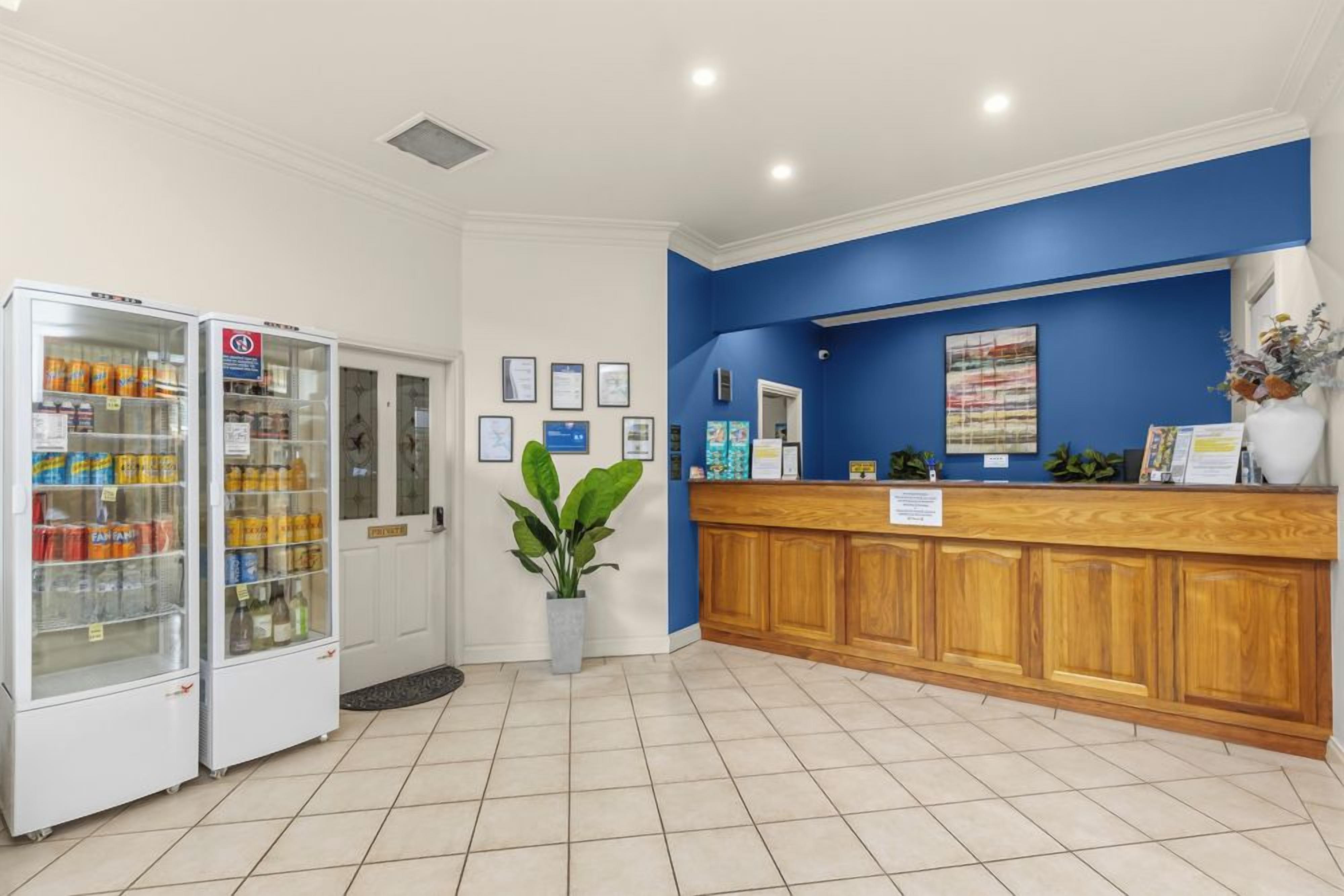 A reception area with a blue wall, wooden reception desk, and two refrigerated beverage dispensers.
