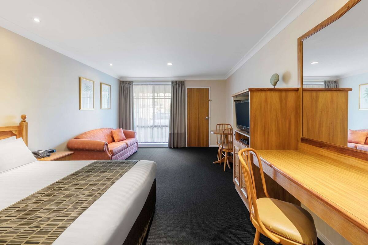 A hotel room with a bed, a sofa, a desk with a TV, and a large mirror.