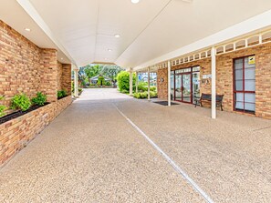 A covered walkway with brick walls, a bench, and a building entrance with glass doors.