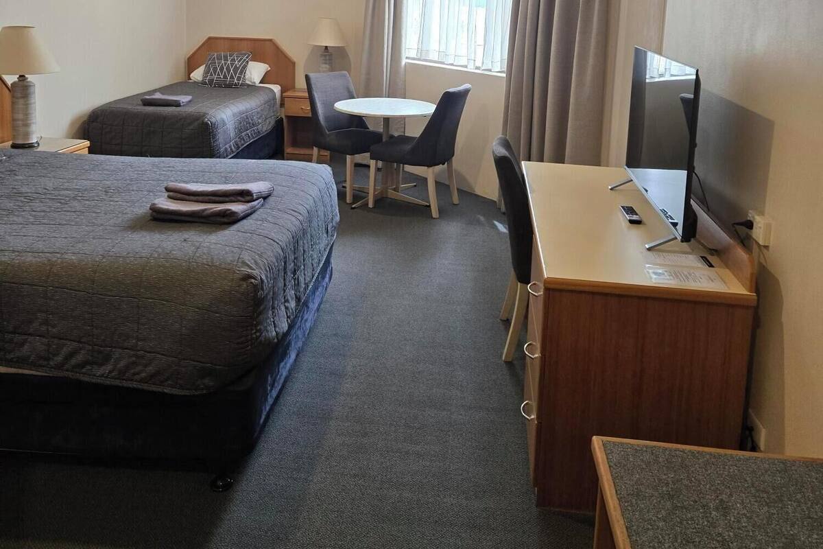 Une chambre d’hôtel avec deux lits, un bureau, une chaise, une télévision et une fenêtre avec des rideaux.