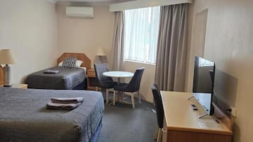 A hotel room with two beds, a desk, a chair, a television, and a window with curtains.