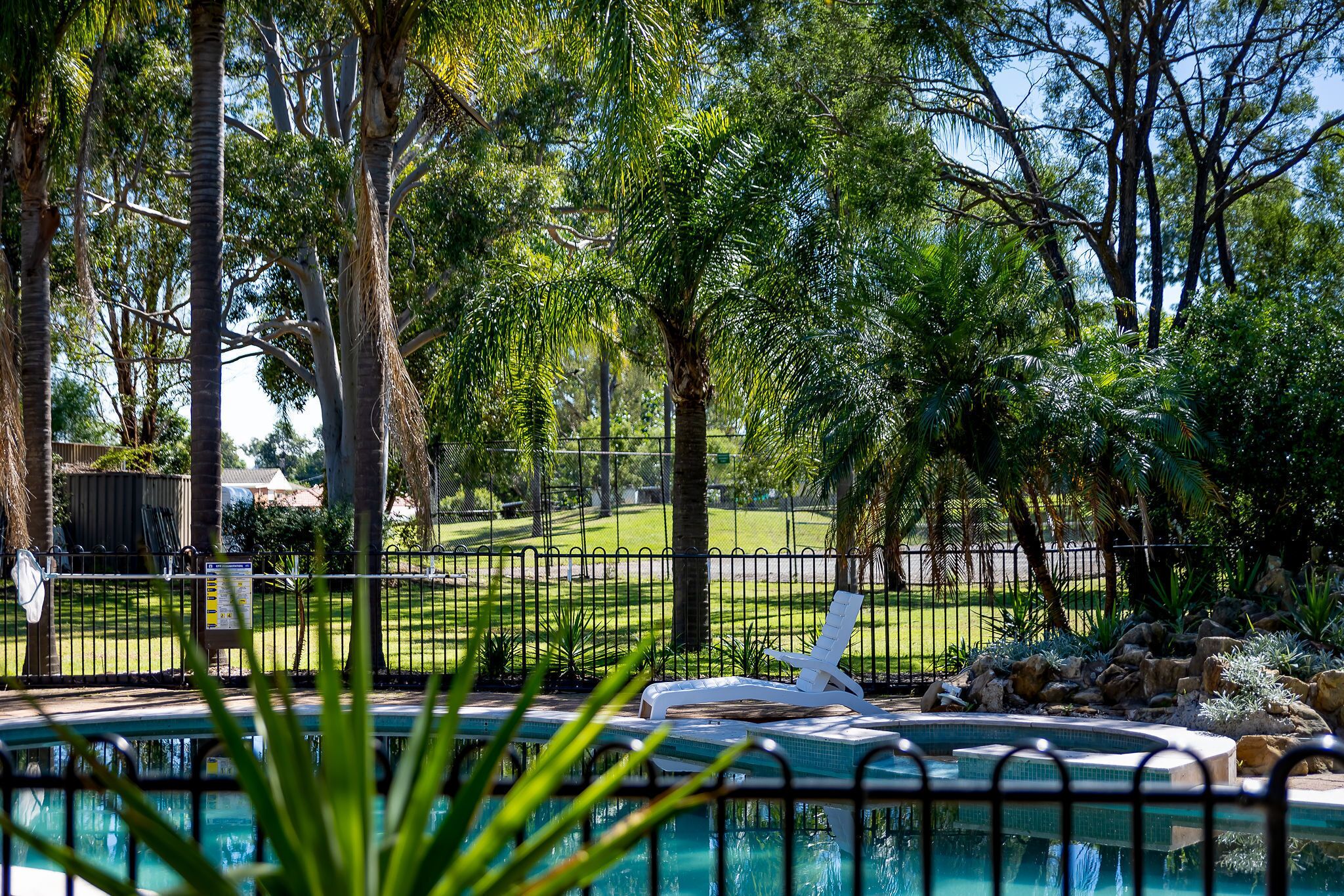 A pool area with a lounge chair, surrounded by trees and a fenced lawn.