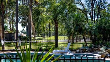 A pool area with a lounge chair, surrounded by trees and a fenced lawn.