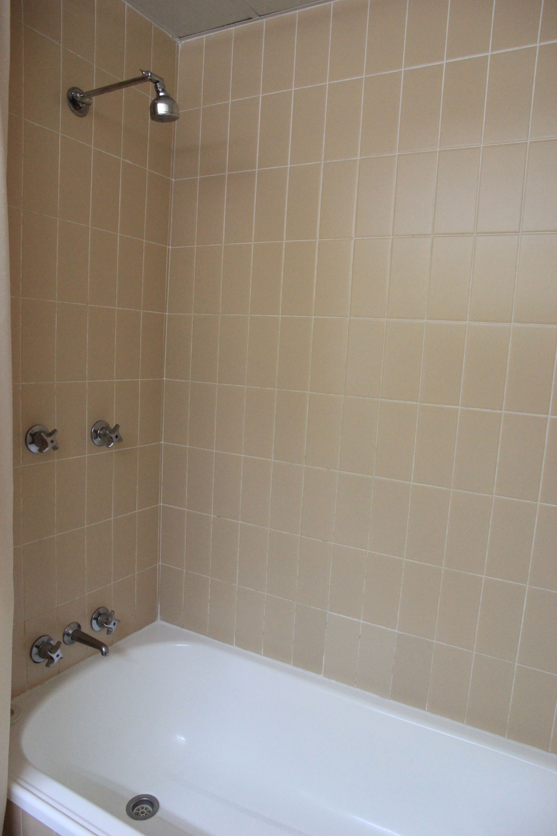 A bathroom with beige tiled walls, a white bathtub, and a showerhead.