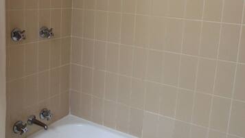 A bathroom with beige tiled walls, a white bathtub, and a showerhead.