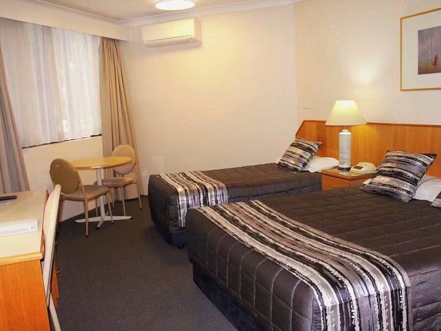 A hotel room with two beds, a desk, a chair, a lamp, and a painting on the wall.