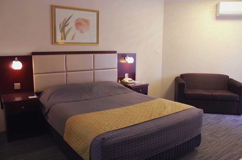 A hotel room with a bed, two bedside tables, a chair, and a wall-mounted air conditioner.