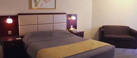 A hotel room with a bed, two bedside tables, a chair, and a wall-mounted air conditioner.