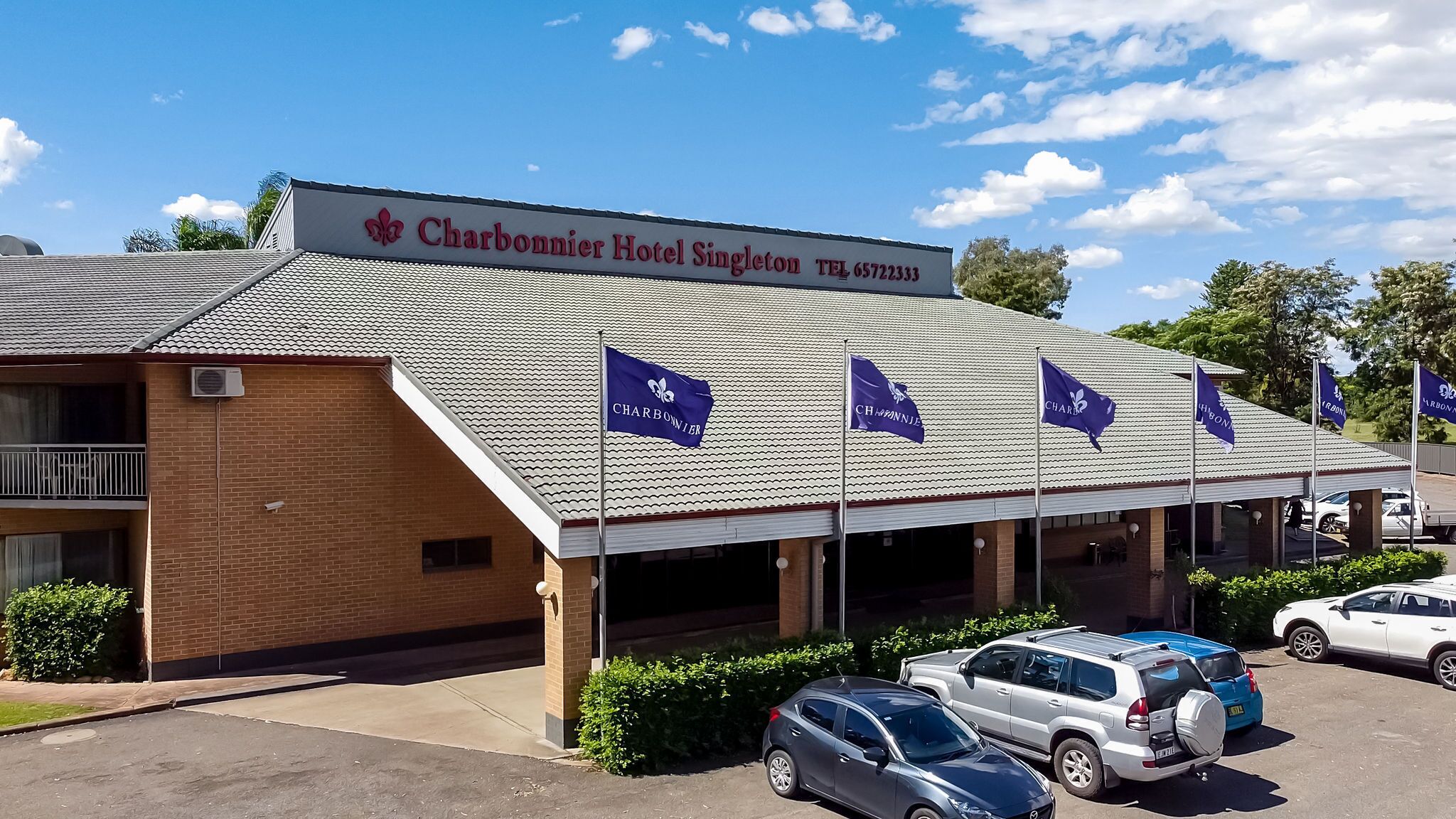 Hotel Charbonnier Singleton met pannendak, meerdere vlaggen en verschillende geparkeerde auto's.