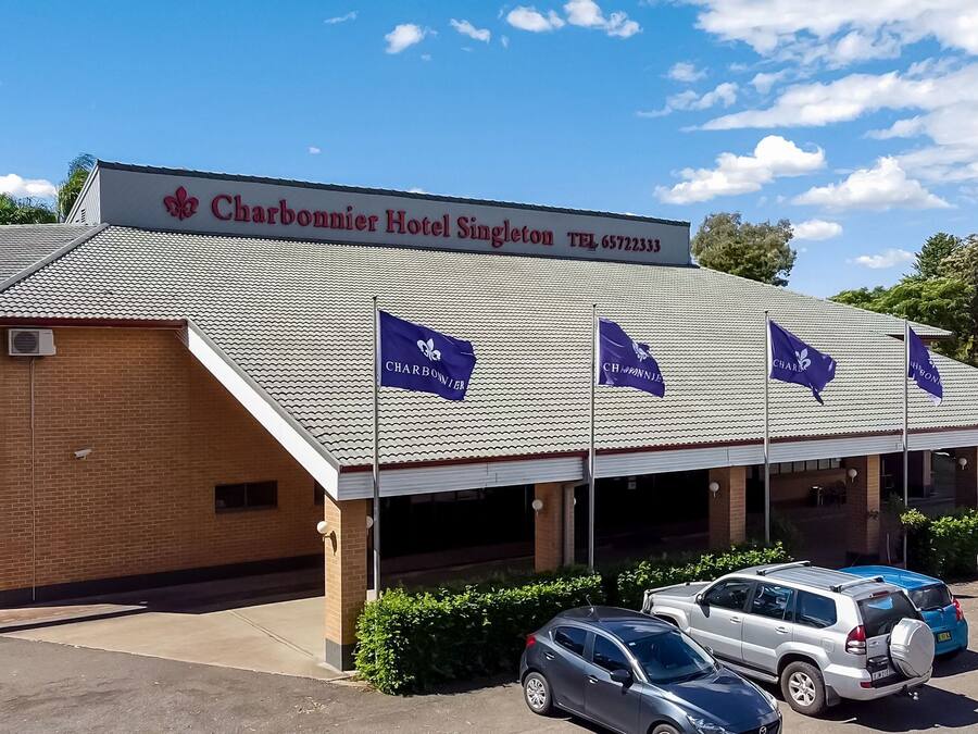 Hotel Charbonnier Singleton met pannendak, meerdere vlaggen en verschillende geparkeerde auto's.