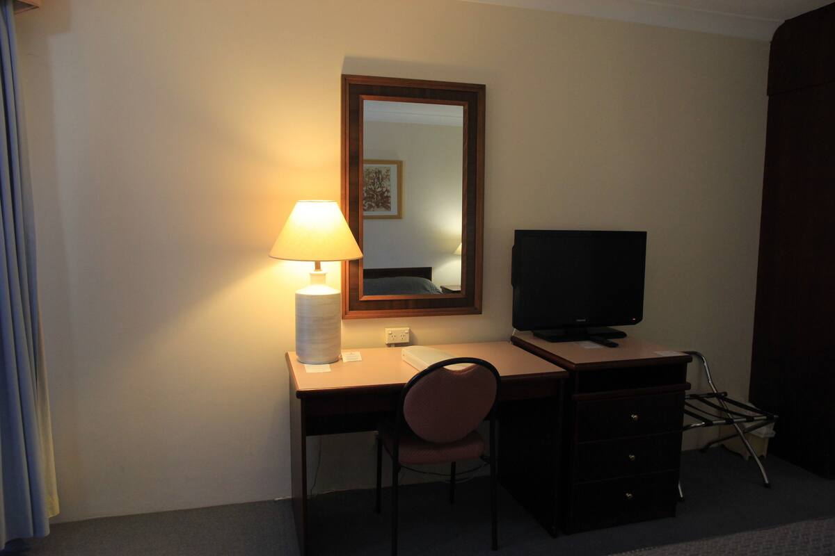 Une chambre d’hôtel équipée d’un bureau, d’une chaise, d’une télévision, d’une lampe et d’un miroir.