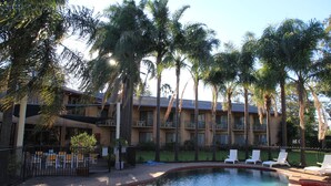 A hotel with a swimming pool, palm trees, and outdoor seating.