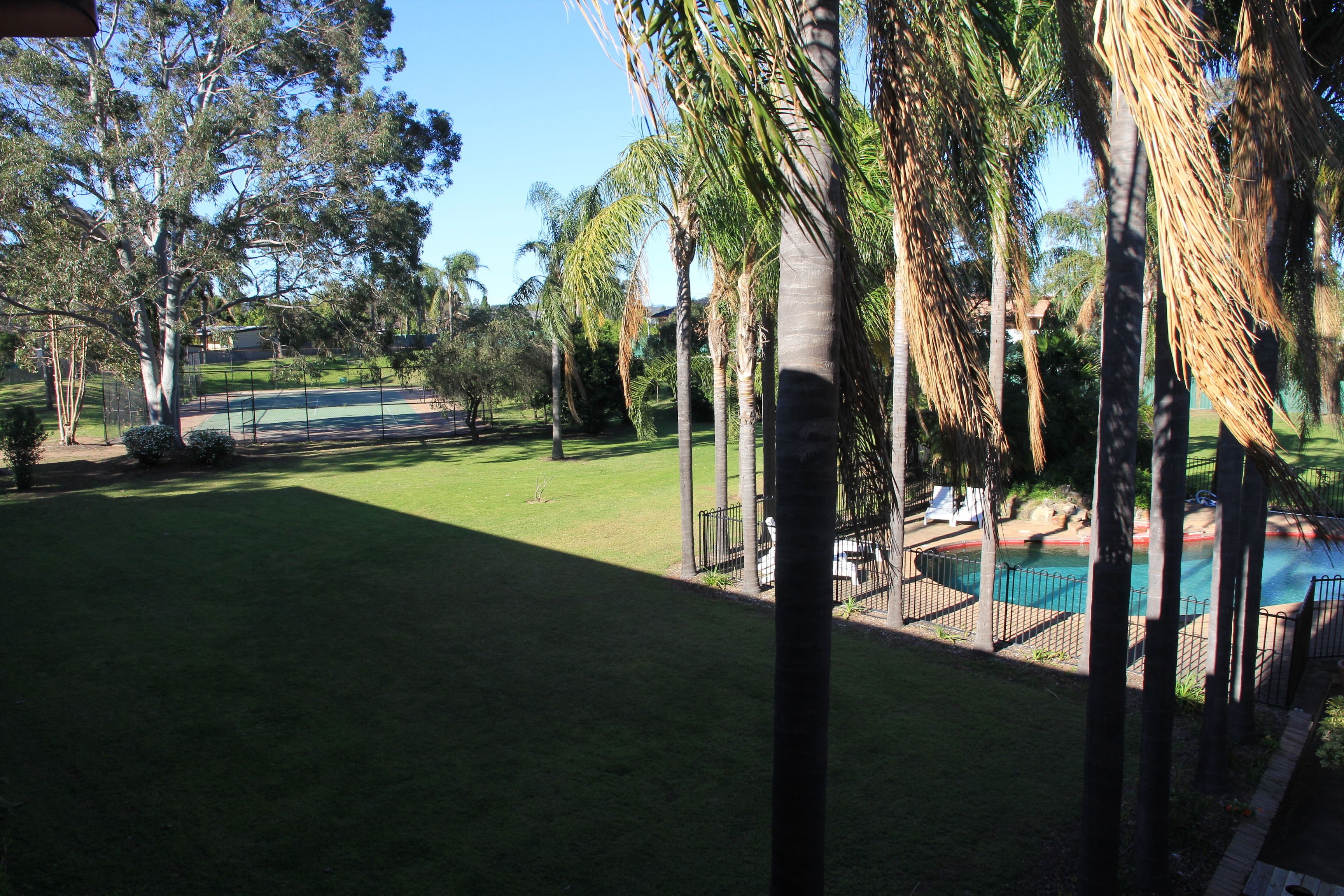 Ein Garten mit Swimmingpool, Palmen und Tennisplatz.