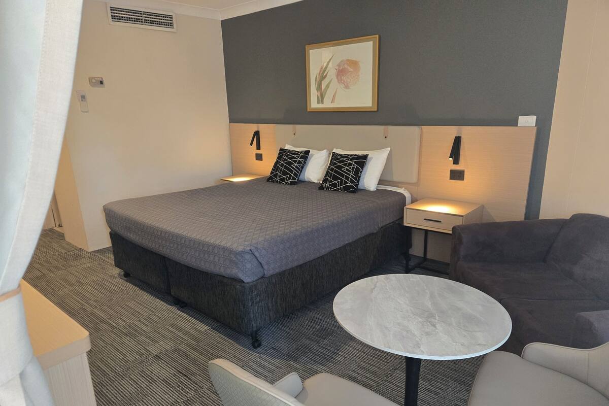Une chambre d’hôtel avec un grand lit, des tables de chevet, une petite table ronde et un canapé.
