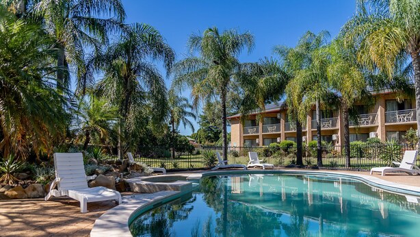 A swimming pool with lounge chairs, surrounded by palm trees and a building with balconies.