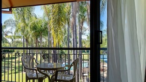A balcony with a table and chairs, overlooking a pool and palm trees. - Charbonnier Motor Inn (Singleton)