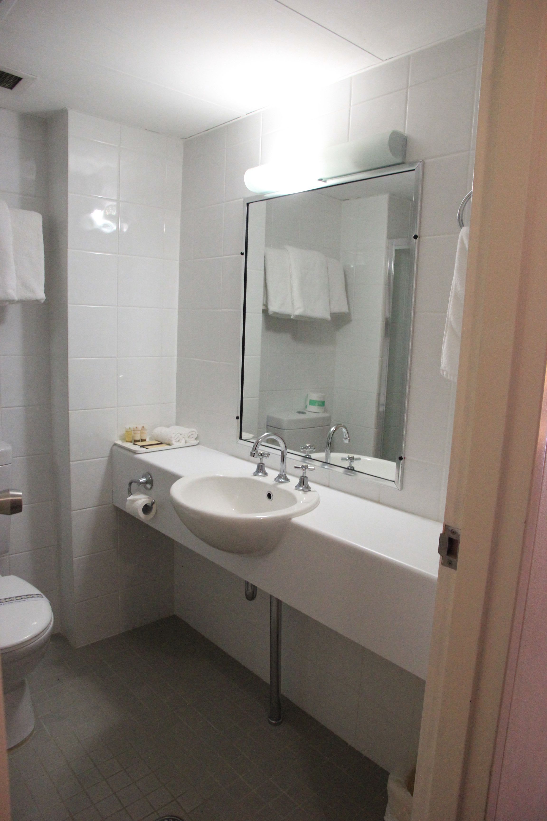 Un baño con lavamanos, espejo e inodoro blancos.
