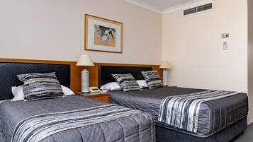 A hotel room with two beds, each with a striped bedspread, a nightstand with a lamp, and a framed picture on the wall.
