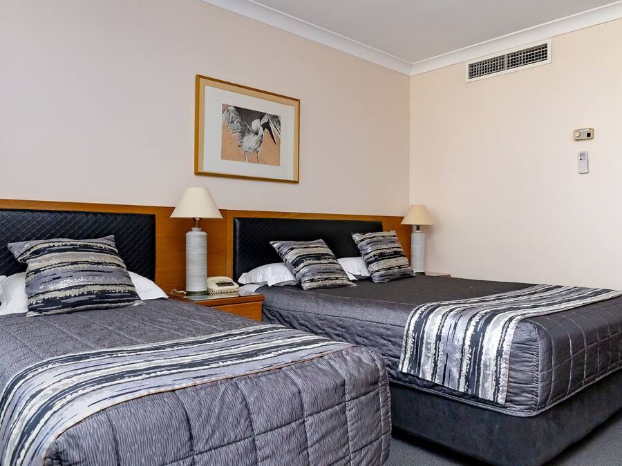 A hotel room with two beds, each with a striped bedspread, a nightstand with a lamp, and a framed picture on the wall.