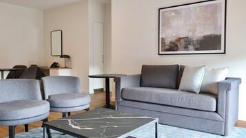 Un soggiorno moderno con un divano grigio, due poltrone, un tavolino da caffè e un grande quadro astratto appeso alla parete.