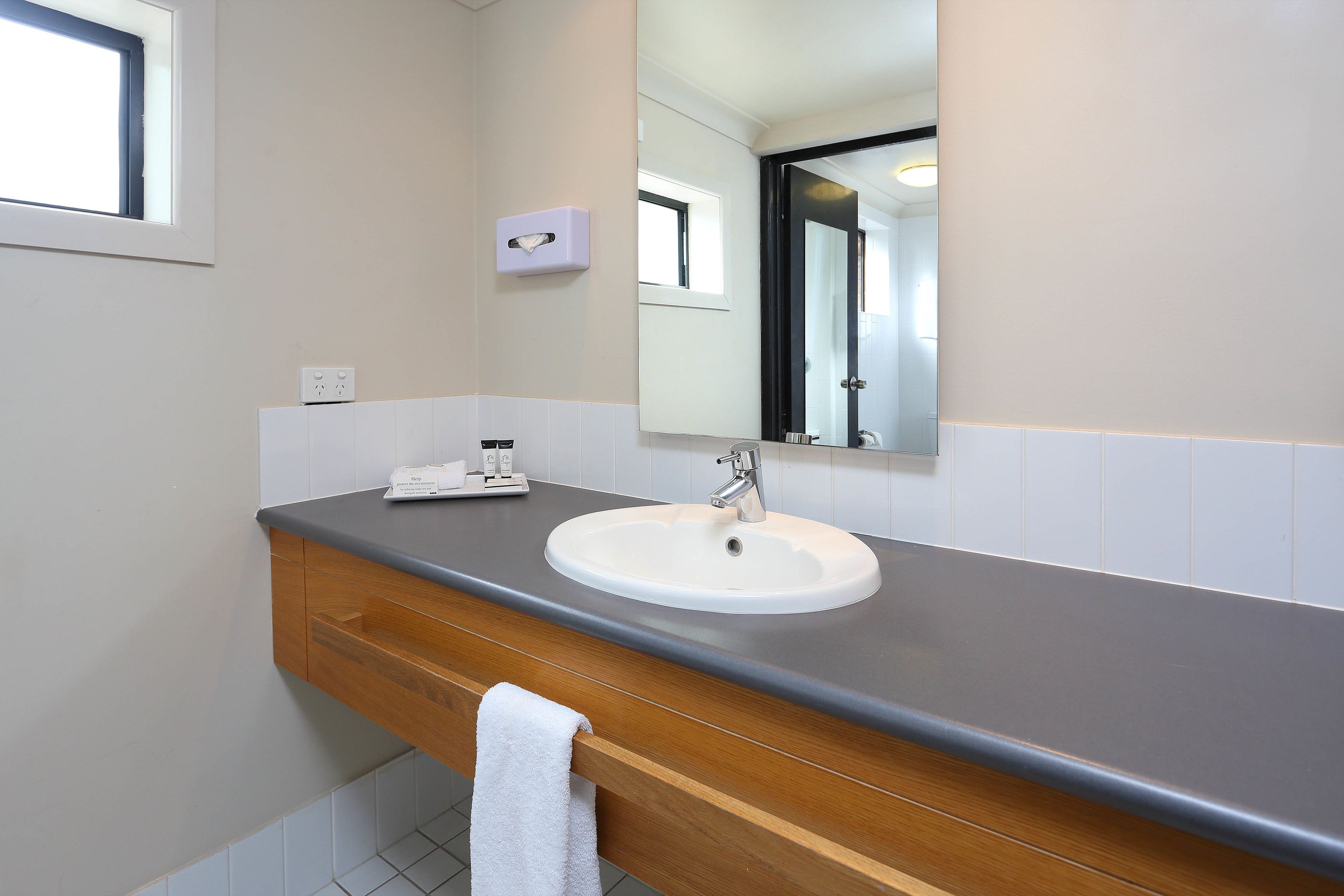 A bathroom with a white sink, a wooden vanity, a mirror, and a window.